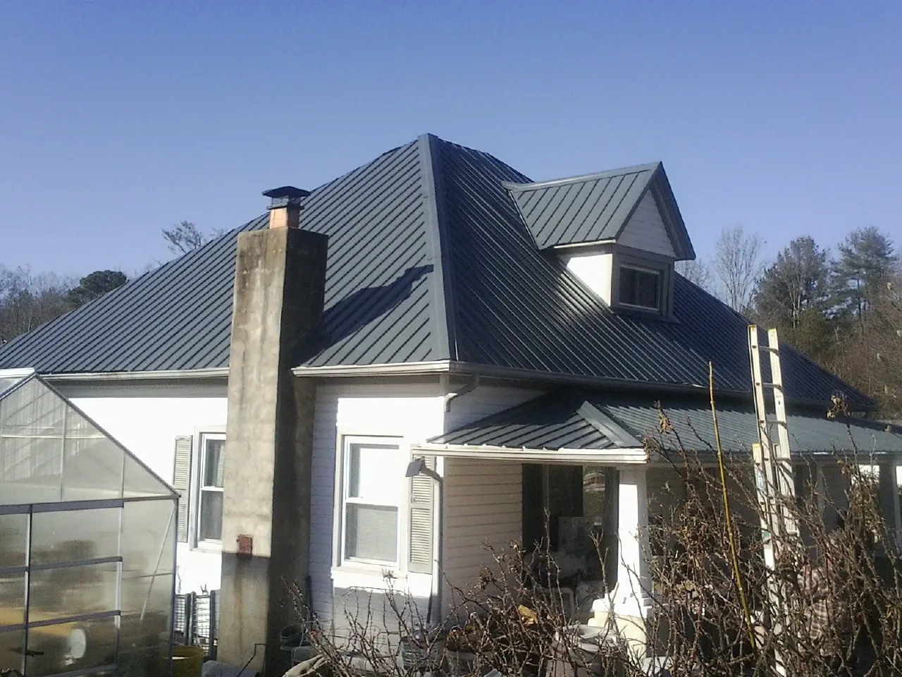 Dark blue standing seam metal roof on a white farmhouse with dormer — Slate & Tile Roof Repair by Roofing Brothers in Spurger