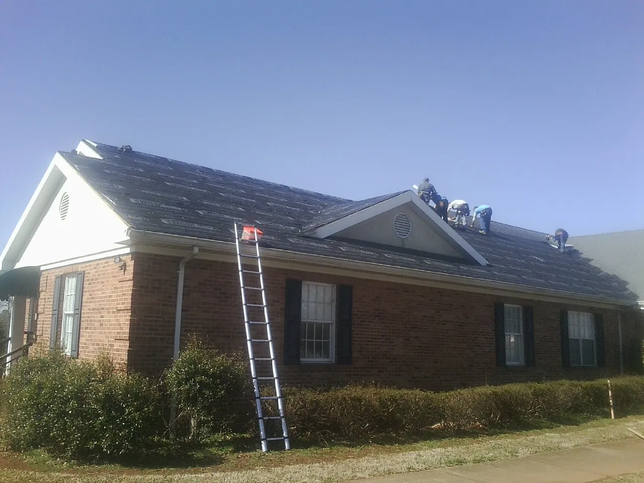 Crew tearing shingles off a brick ranch roof with a ladder set — Emergency Roof Repair work by our crew in Spurger