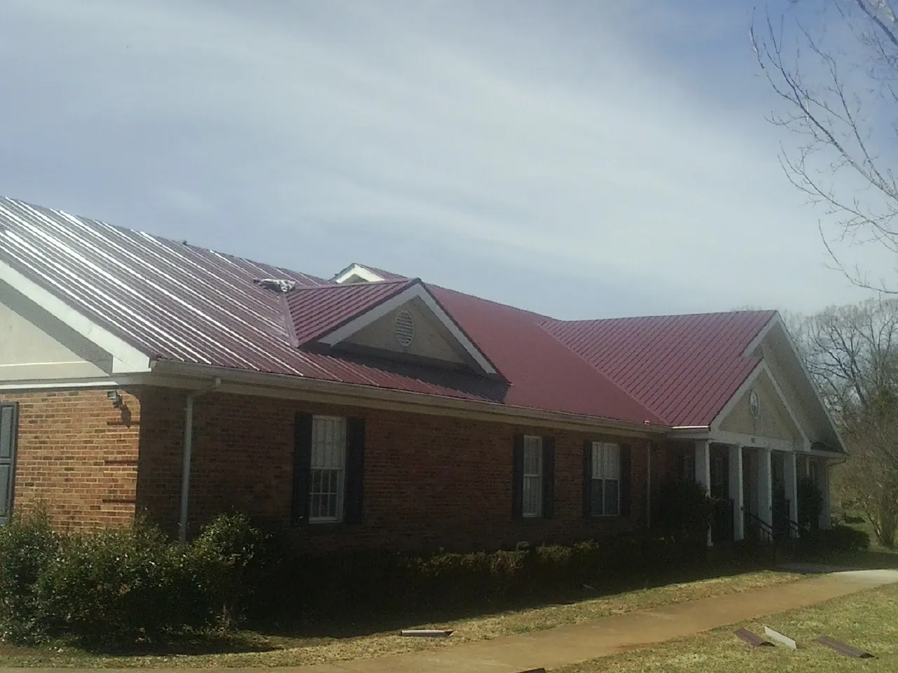 Red metal roof with gabled entries on a long brick building, from a Hail Damage Roof Repair job in Spurger
