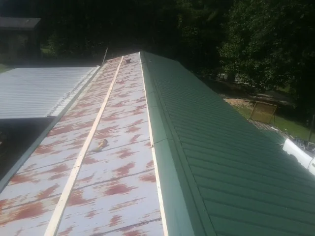 Old rusted panels beside newly installed green metal roofing — Wind Damage Roof Repair by Roofing Brothers in Spurger