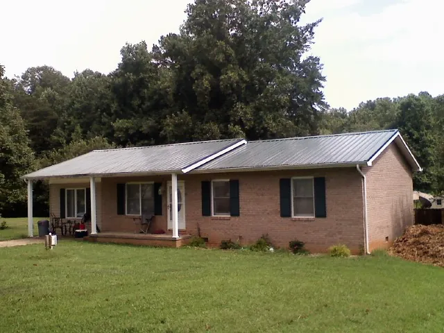 Gray metal roof on a brick ranch house with a side carport in Spurger