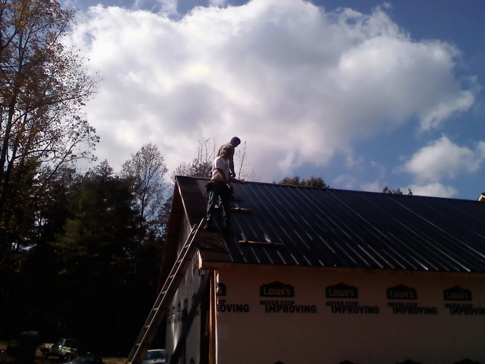 Roofer fastening dark metal panels high against a cloudy sky, from a Roof Inspection job in Spurger