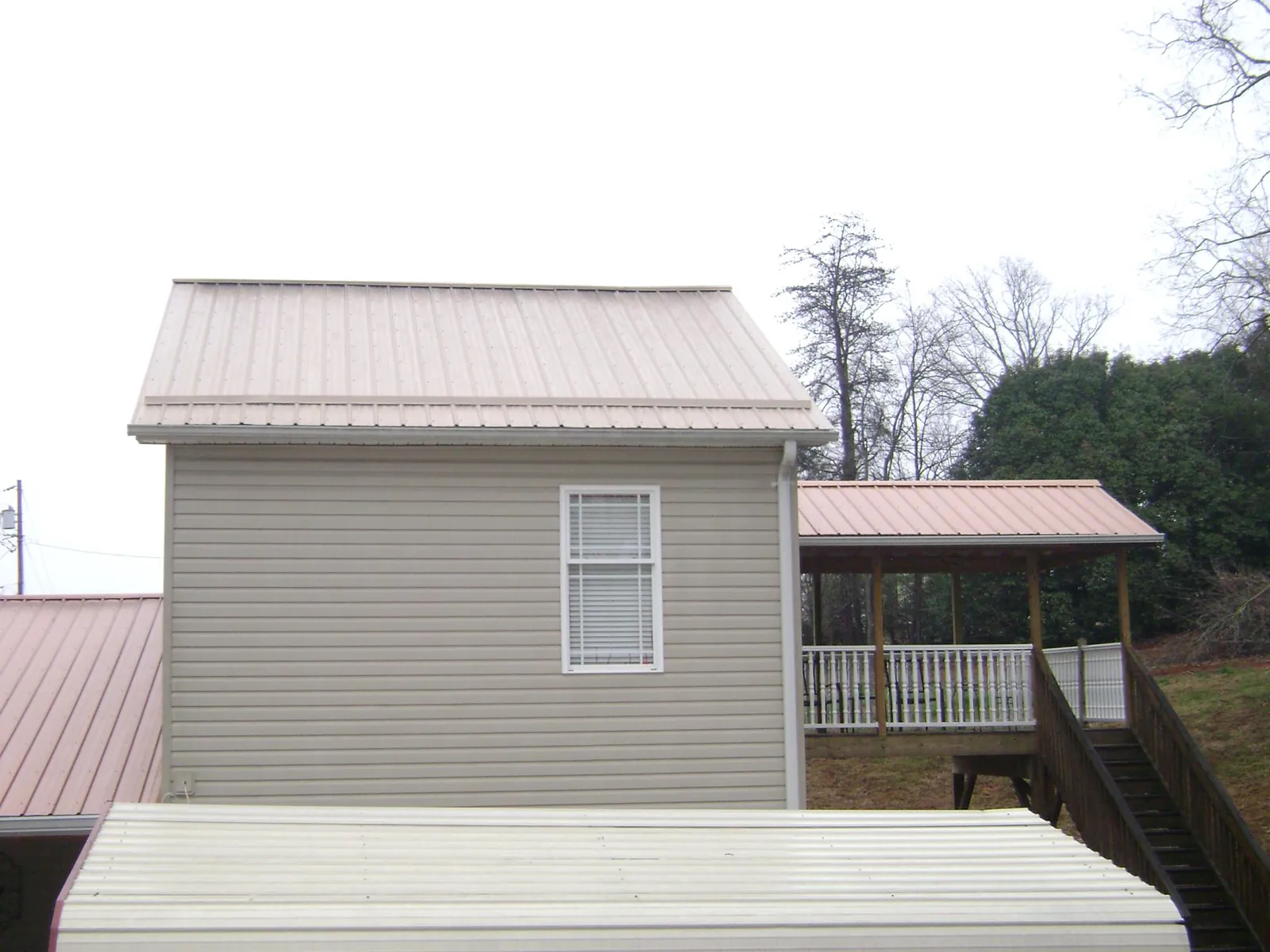 Tan metal roofs on a two story addition and attached porch, from a Roof Replacement job in Spurger